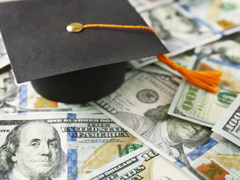 A graduation cap sits atop a pile of dollar bills.
